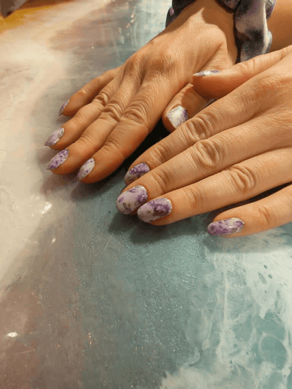 Both hands showing purple floral nail wraps with rose pattern design