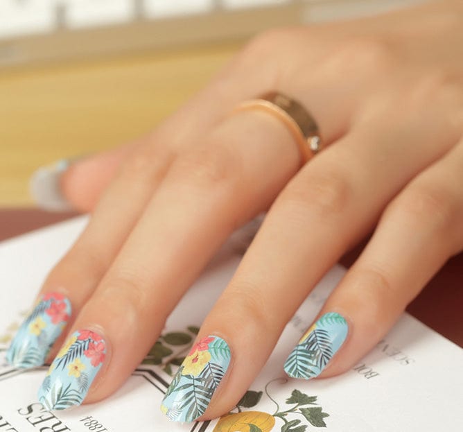 Hand wearing tropical nail wraps with blue palm leaves and coral hibiscus flowers at-home manicure