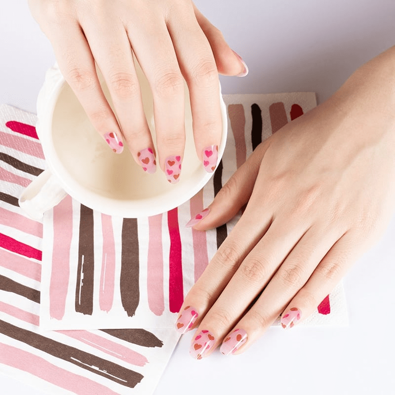 Both hands displaying pink heart pattern nail wraps for complete Valentine's Day nail art look