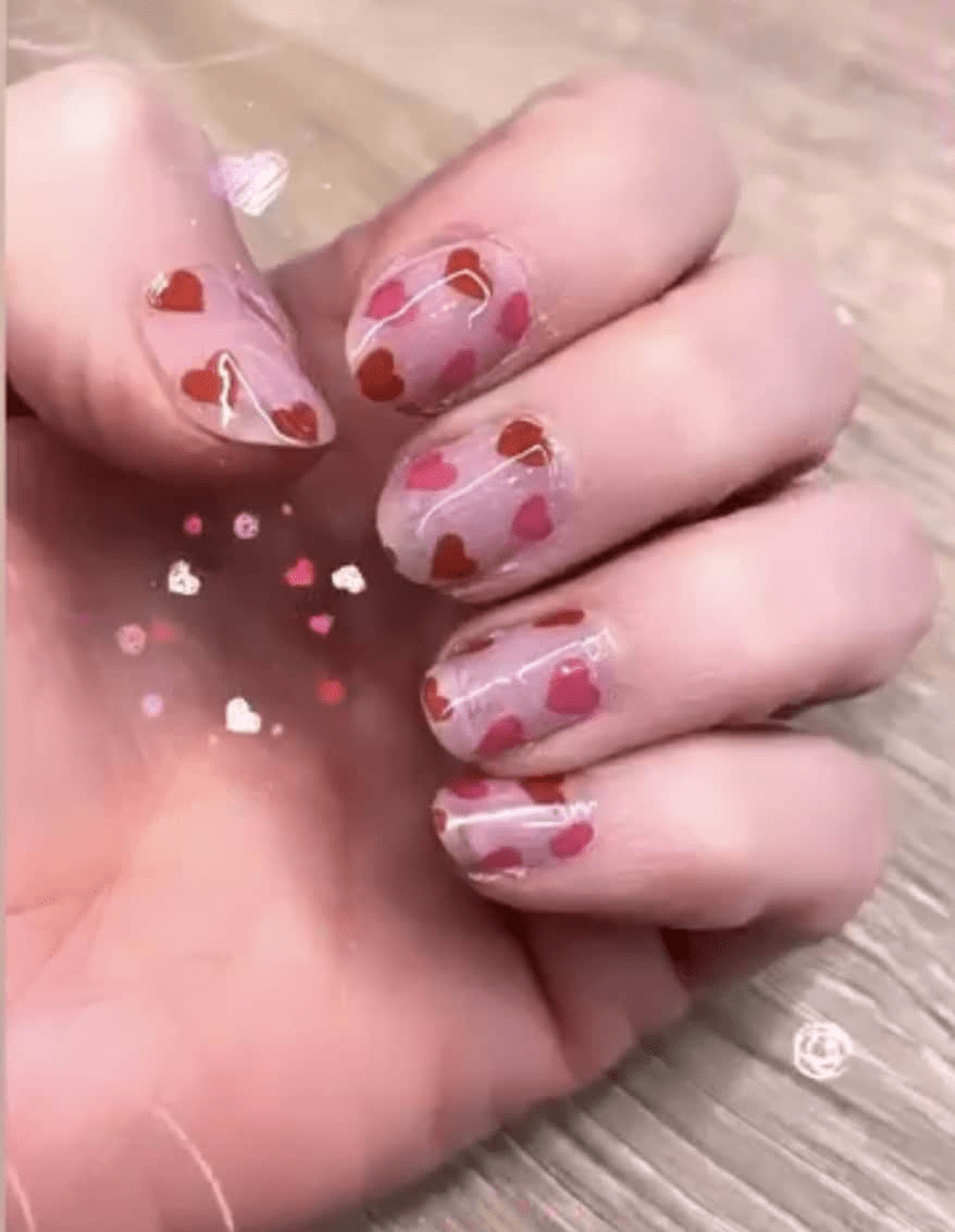 Pink heart pattern nail wraps on hand showing Valentine's Day nail art design