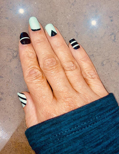 Hands displaying mint green black striped geometric nail art wraps manicure