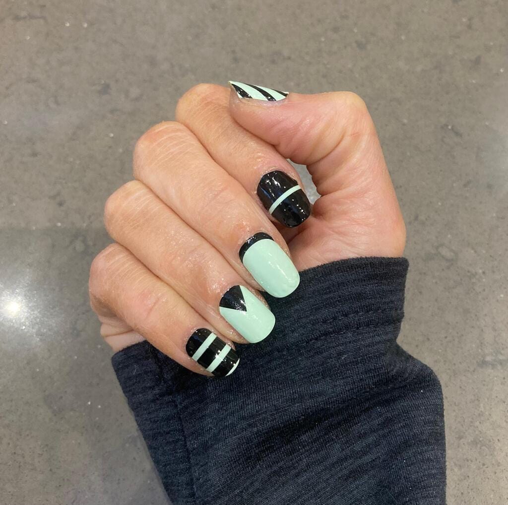 Hand wearing mint green and black geometric nail wraps with triangle patterns