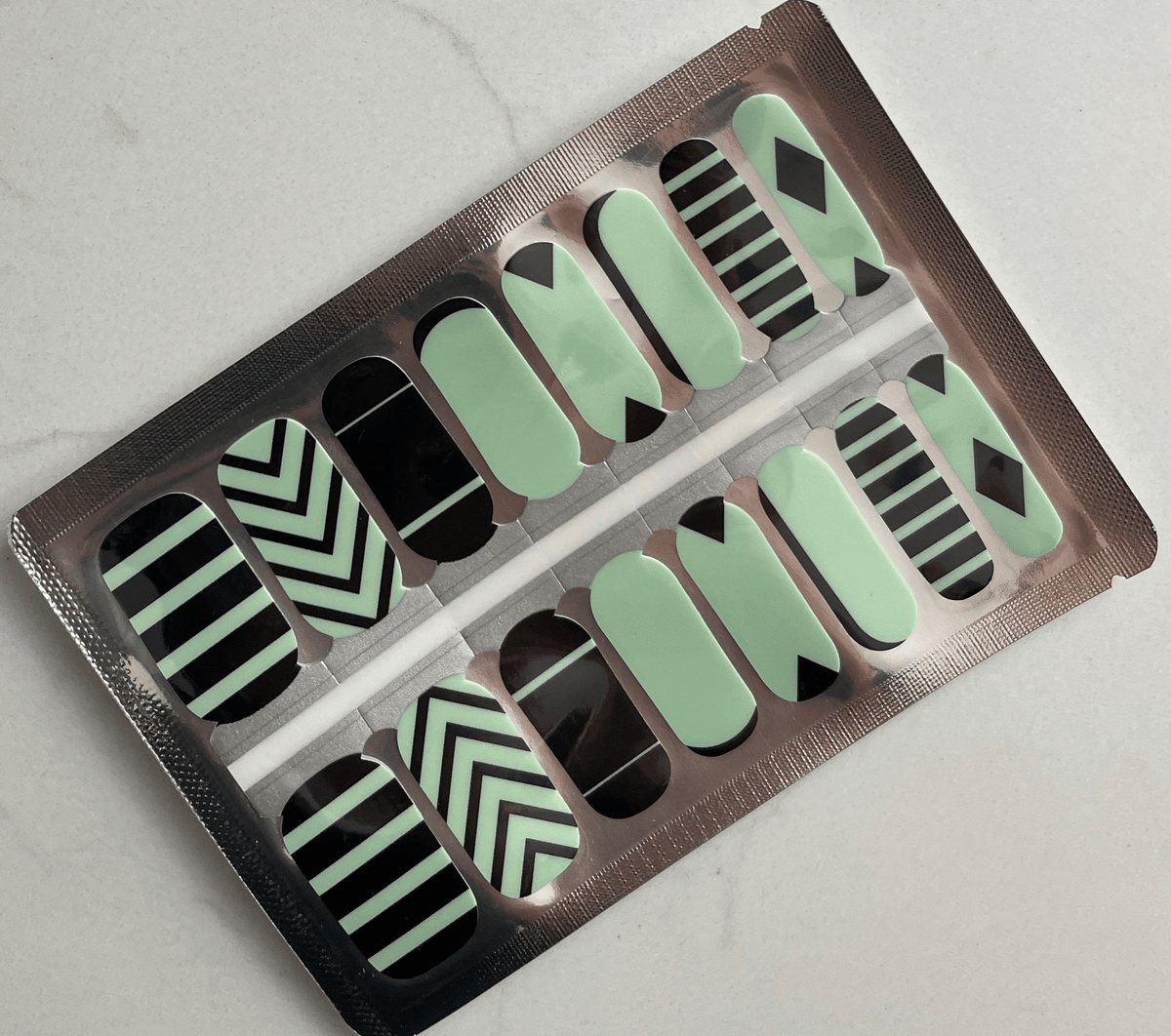 Green and black geometric nail wraps with chevron stripes and triangular patterns in packaging