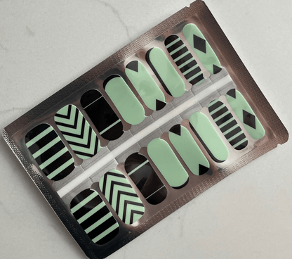 Green and black geometric nail wraps with chevron stripes and triangular patterns in packaging