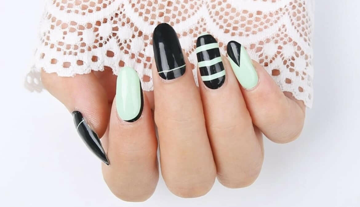 Black and mint green geometric nail wraps with striped patterns on hand