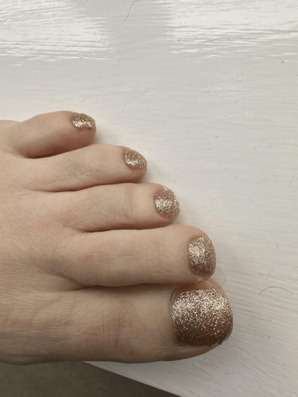 Foot wearing gold glitter pedicure nail wraps on toes for sparkly nail art
