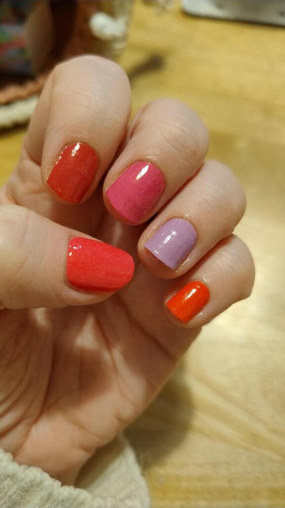 Vibrant coral pink purple nail wraps on hand displaying glossy berry shade manicure