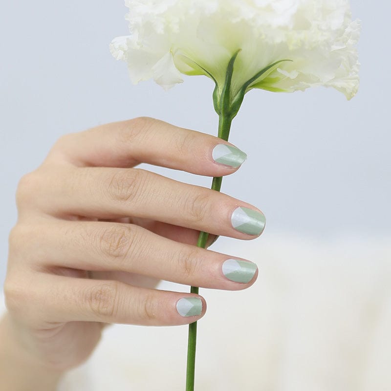 Hand holding white flower with sage green nail wraps manicure