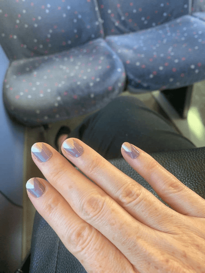 Hand wearing brown and gold geometric nail wraps in car showing chevron pattern design