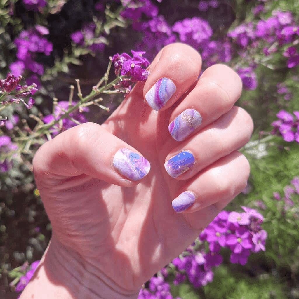 Purple and blue marble nail wraps with gold glitter accents on short round nails