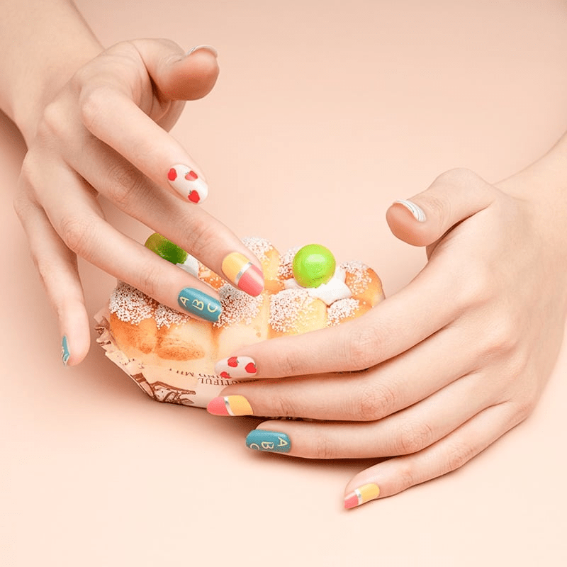 Cupped hands displaying colourful apple pattern nail wraps with red hearts and multicoloured designs