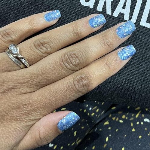 Blue glitter nail wraps on hand with silver ring showing festive manicure