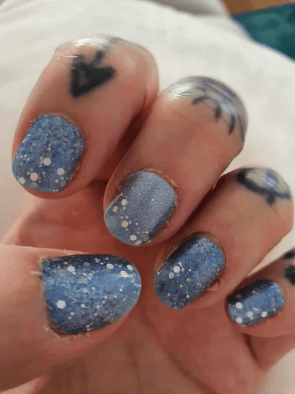 Blue glitter nail wraps with silver dots on hand creating winter nail art
