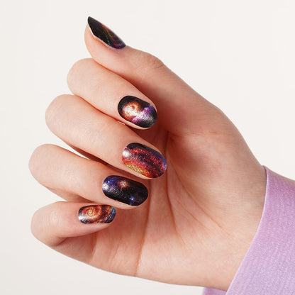 Hand wearing cosmic space nail wraps featuring galaxy nebula patterns purple orange