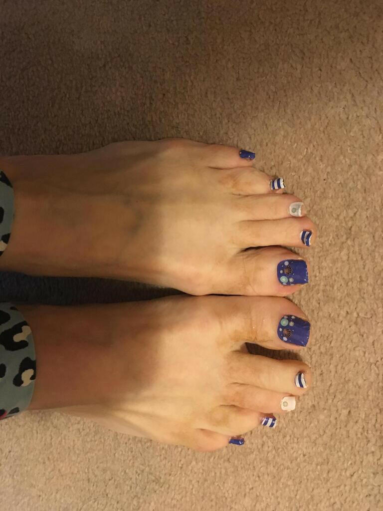 Feet wearing blue pedicure nail wraps with white shells and nautical beach pattern