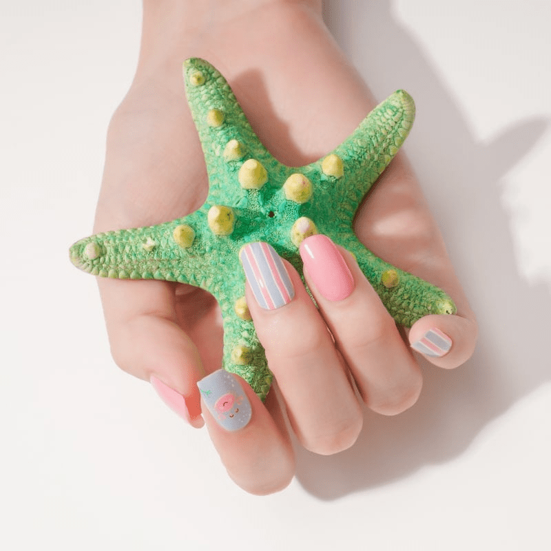Hand holding green starfish wearing coral pink and striped nail wraps with beach motifs