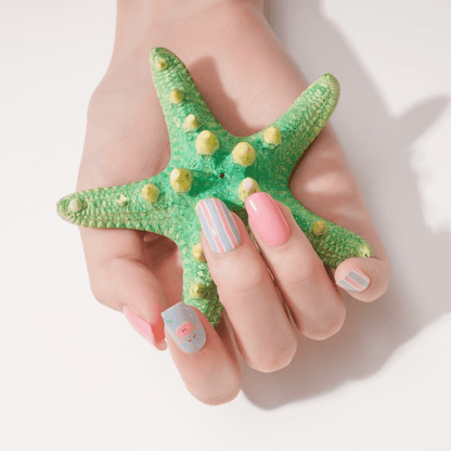 Hand holding green starfish wearing coral pink and striped nail wraps with beach motifs