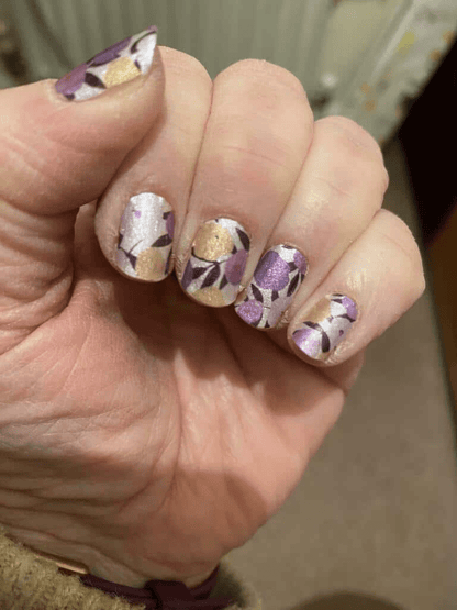 Hand displaying purple and yellow floral nail wraps manicure with abstract botanical pattern