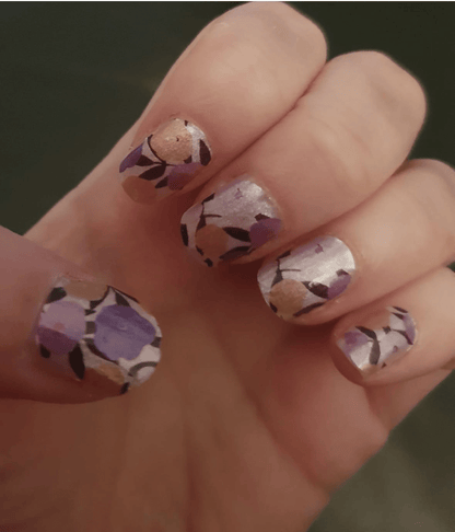 Hand showing purple floral nail wraps with yellow flowers on glossy finish nails