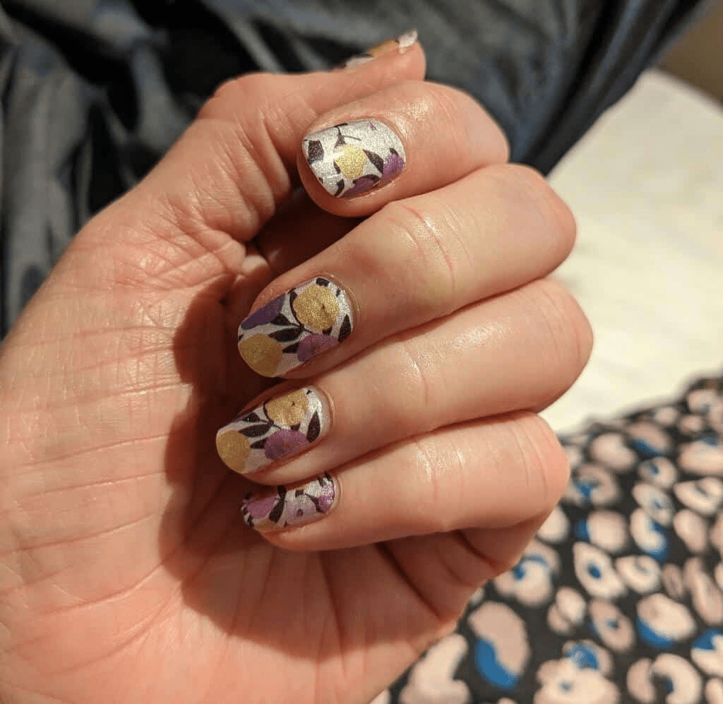 Hand displaying purple and yellow floral pattern nail wraps for spring manicure design