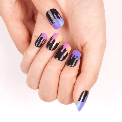 Hands displaying vibrant gradient nail wraps featuring black paint drip nail art design