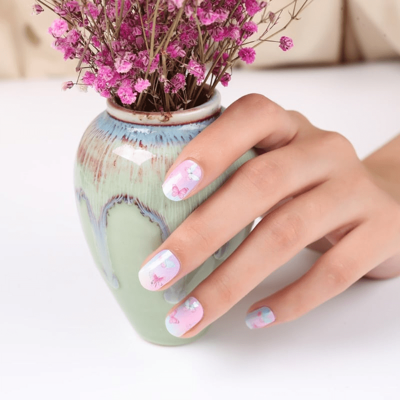 Hand with pink butterfly nail art wraps touching ceramic vase with flowers