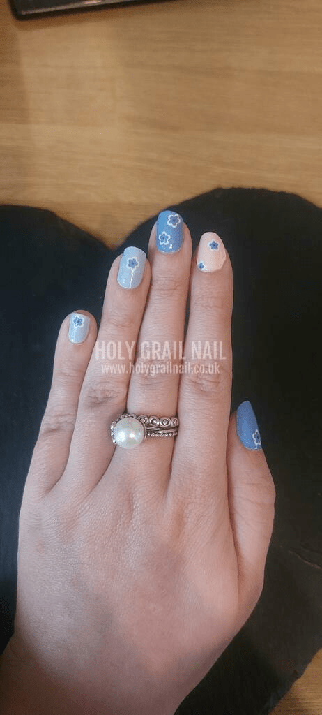 Pastel blue and pink flower nail wraps on hand with white daisy art pattern