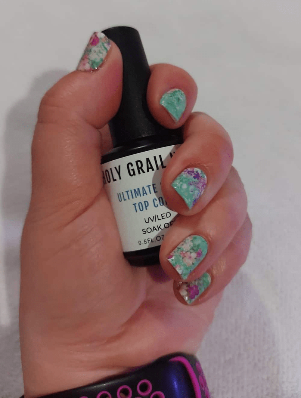 Hand holding topcoat, wearing green nail wraps with pink and white floral print