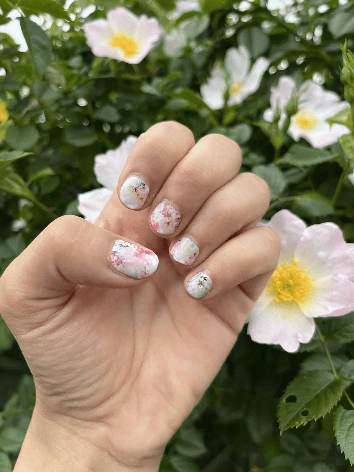 Hand displaying pink floral nail wraps amongst white flowers showcasing spring nail art design