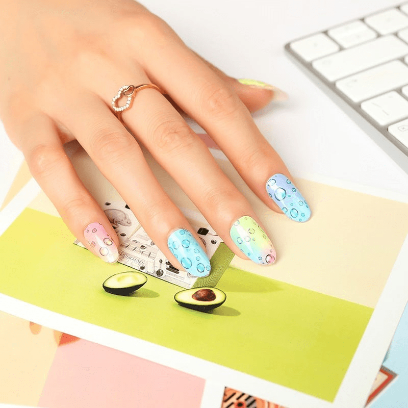 Hand with rainbow bubble nail wraps over keyboard displaying trendy nail art