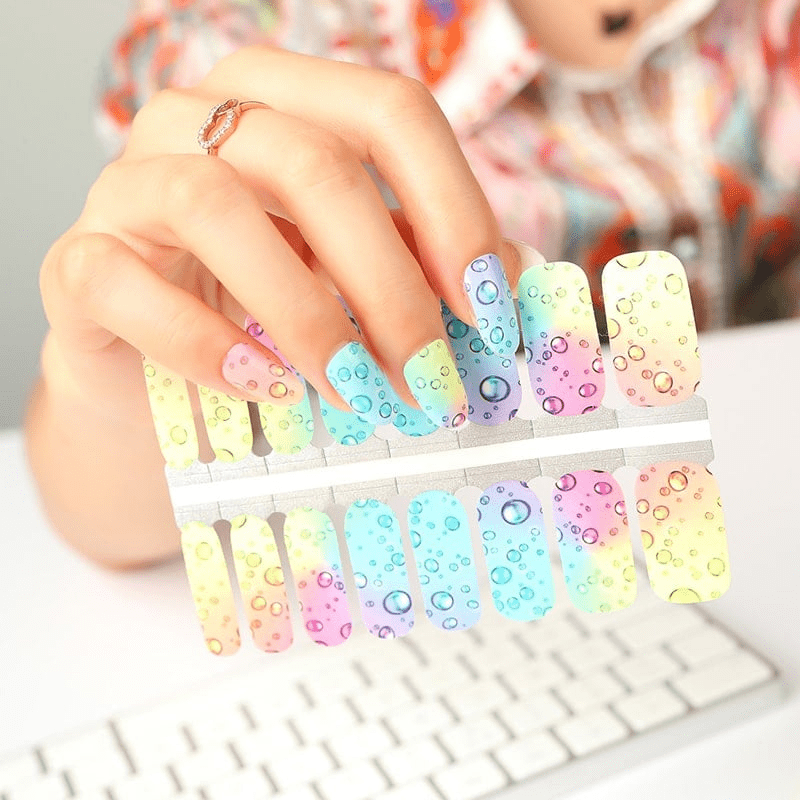 Hands showing pastel gradient nail wraps with bubble pattern manicure design