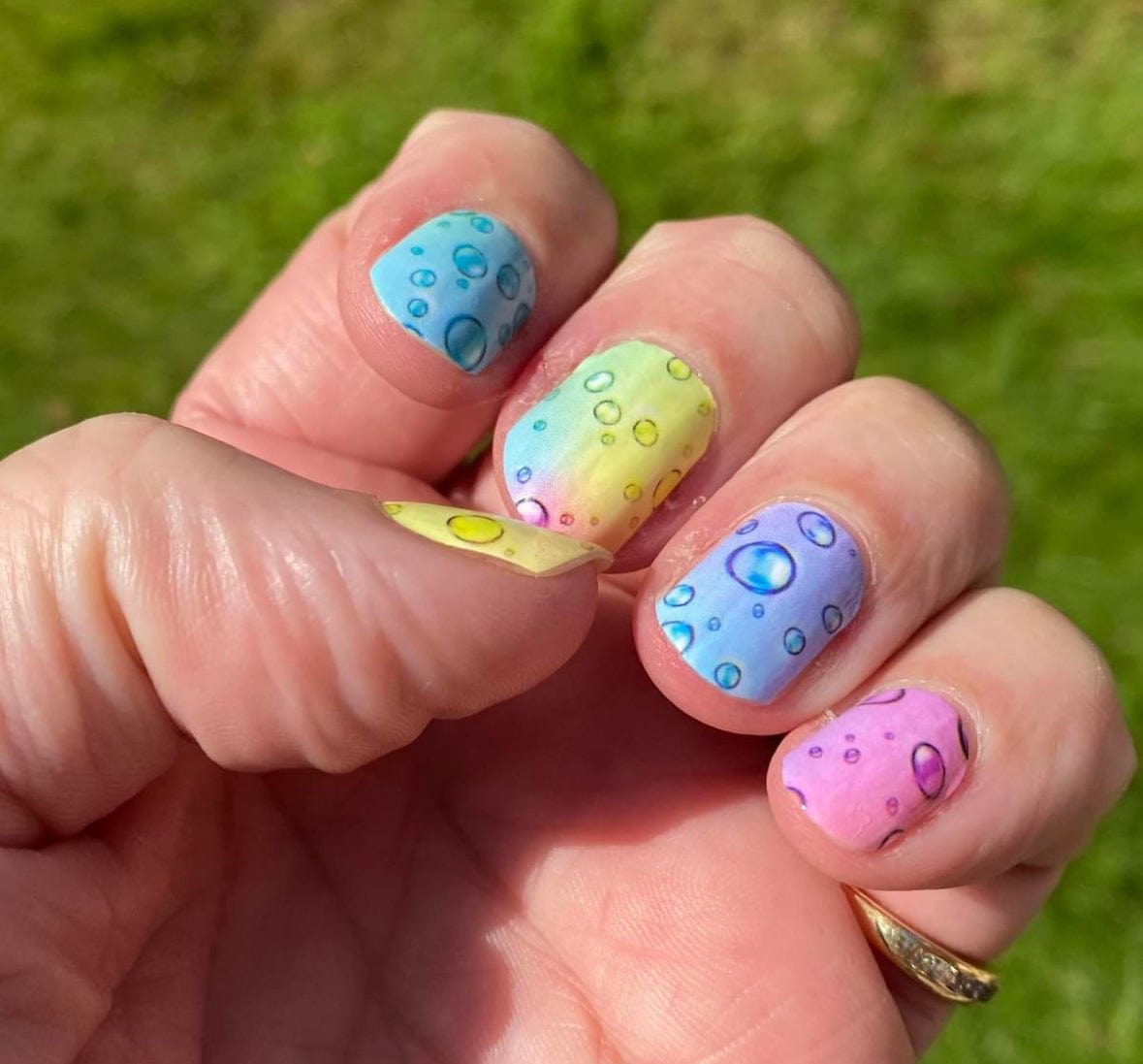 Colourful bubble pop nail wraps on hand featuring blue pink yellow gradient designs