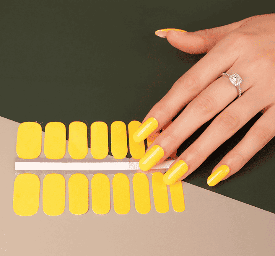 Bright yellow nail wraps applied on hand with matching sheet showing at-home manicure