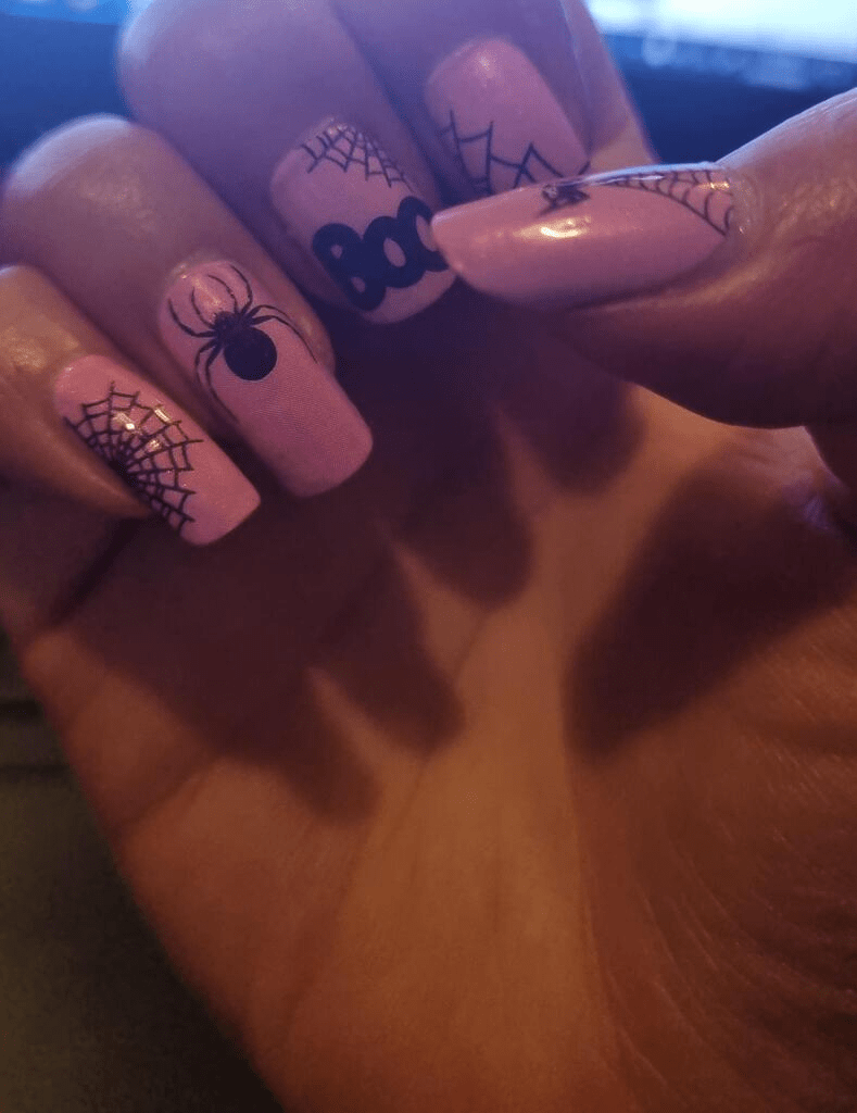 Pink Halloween nail wraps on hand featuring black spiders and cobweb nail art designs