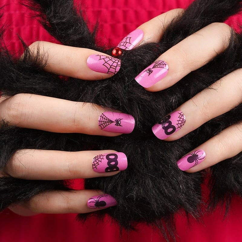 Spooky pink nail wraps with black Halloween spiders and BOO lettering on hands