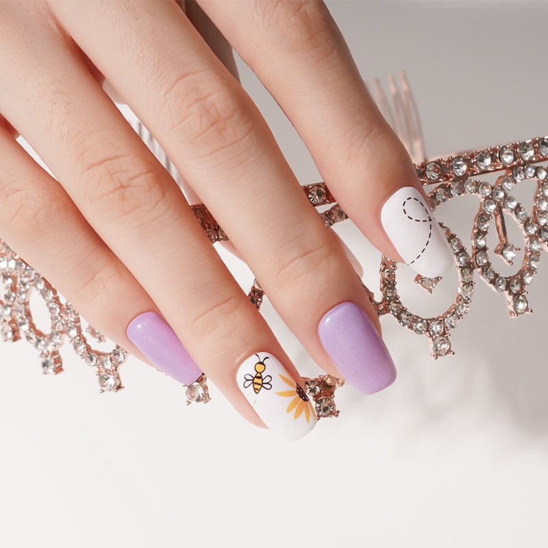 Hand wearing purple nail wraps with white bee accent nails and gold jewellery
