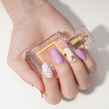 Purple bee nail wraps on hand holding perfume bottle showing at-home manicure