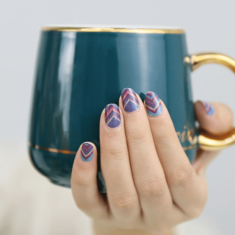Hand holding teal mug displaying blue chevron nail wraps geometric manicure
