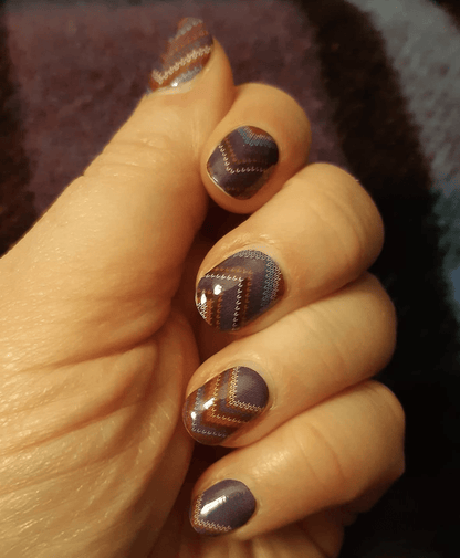 Hand wearing brown cable knit pattern nail wraps with chevron design