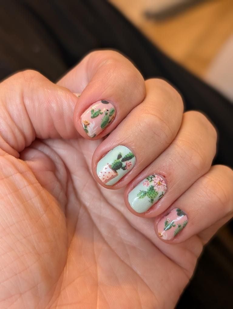 Cactus nail wraps on fingers displaying green botanical manicure with plant patterns