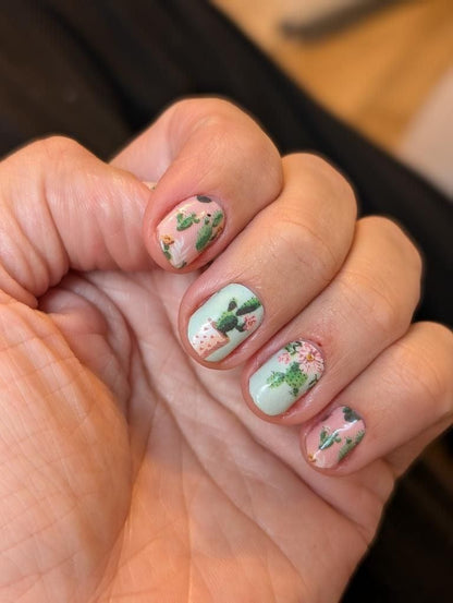 Cactus nail wraps on fingers displaying green botanical manicure with plant patterns