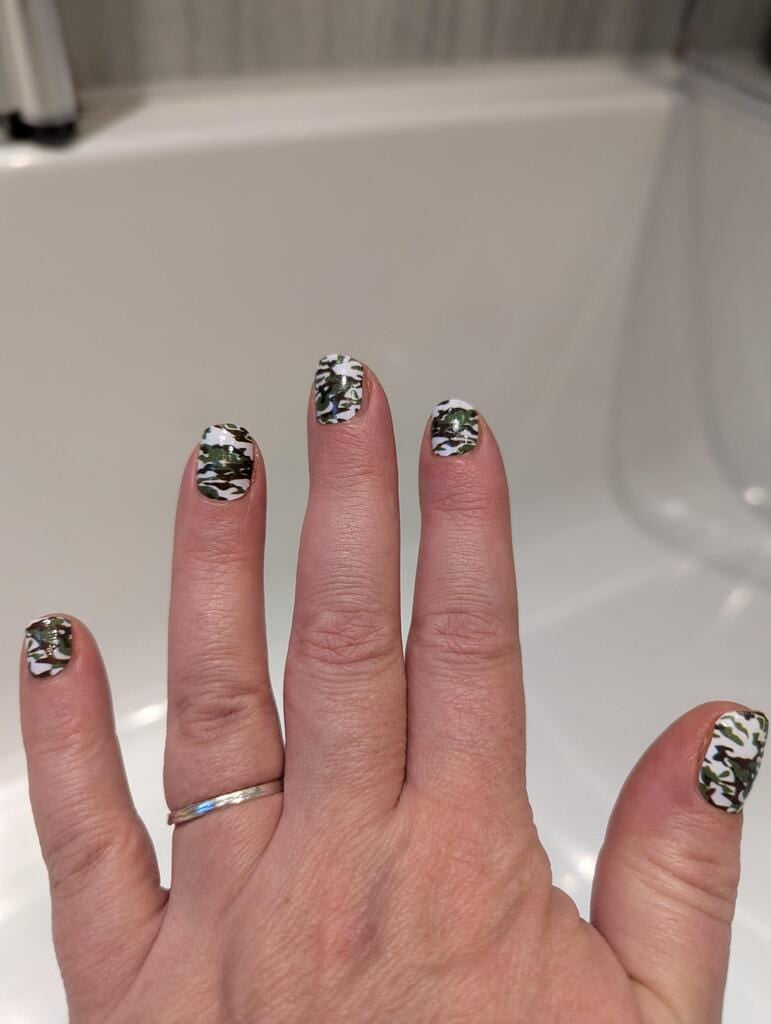 Green camouflage pattern nail wraps on hand showing military-inspired nail art design