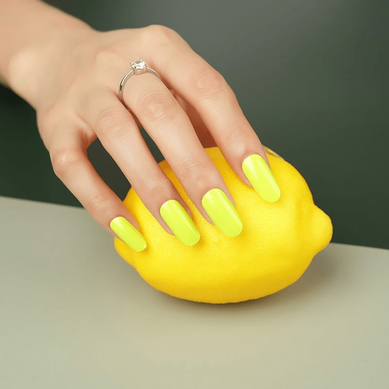 Hand with neon yellow nail wraps holding matching yellow lemon for colour coordination