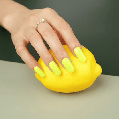 Hand with neon yellow nail wraps holding matching yellow lemon for colour coordination
