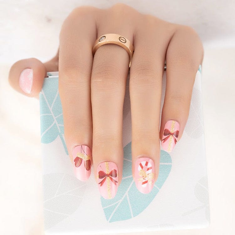 Pink nail wraps with candy cane and ribbon Christmas designs on hand with ring