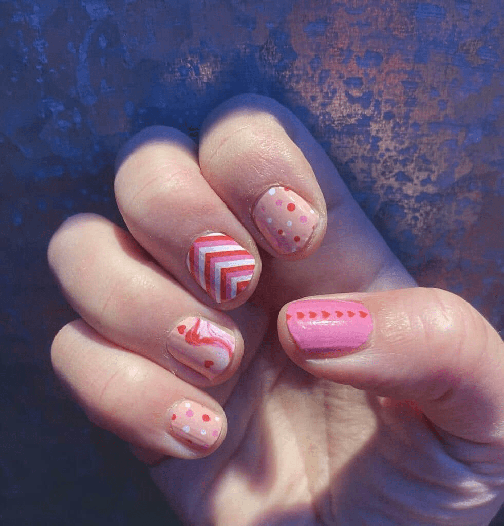 Pink nail wraps manicure on hand featuring hearts stripes and dots nail art