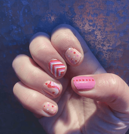 Pink nail wraps manicure on hand featuring hearts stripes and dots nail art