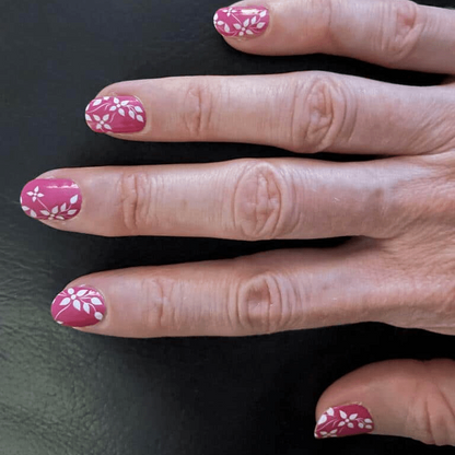 Fingers showing pink nail wraps with delicate white leaf pattern, at-home manicure