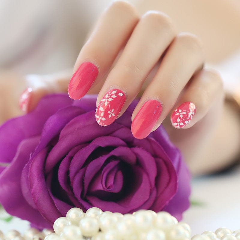Hand with pink floral nail wraps manicure next to purple rose and pearls