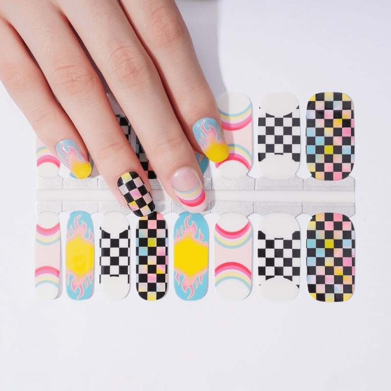 Hand displaying colourful nail wraps with chequered patterns, rainbows and flame designs for at-home manicures